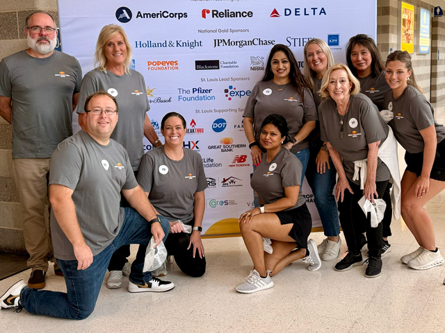 A group of adults posing in front of a sponsor sign for 911 Day in St. Louis.