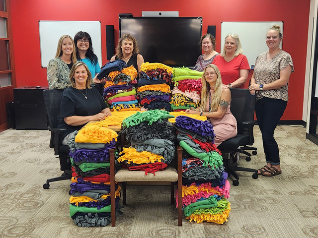A group of adults gathered around a large pile of homemade blankets.