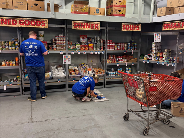 Two adults shelving food at a food pantry.